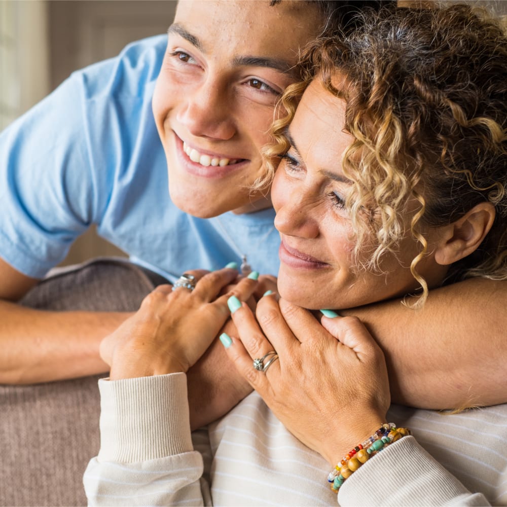 Mother and son smiling together, with the son wrapping his arm around her neck.