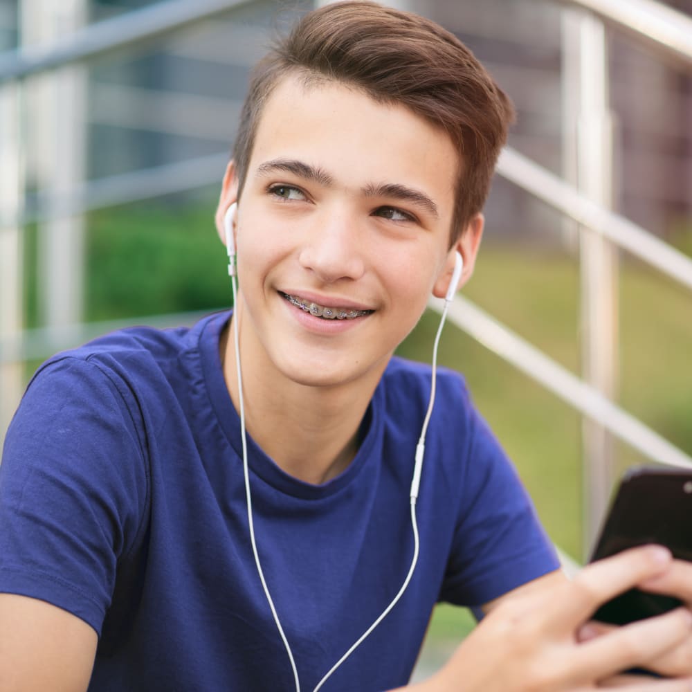 Teenage boy wearing a blue T-shirt, holding his cellphone and listening to music with earphones.