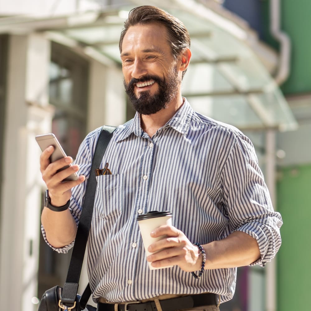 Man with a beard smiling while looking into a handheld mirror at a dental clinic.
