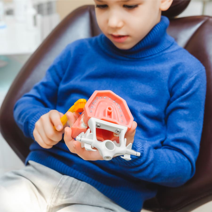 Young girl holding a teddy bear sitting in a dental chair while showing her teeth to the dentist.