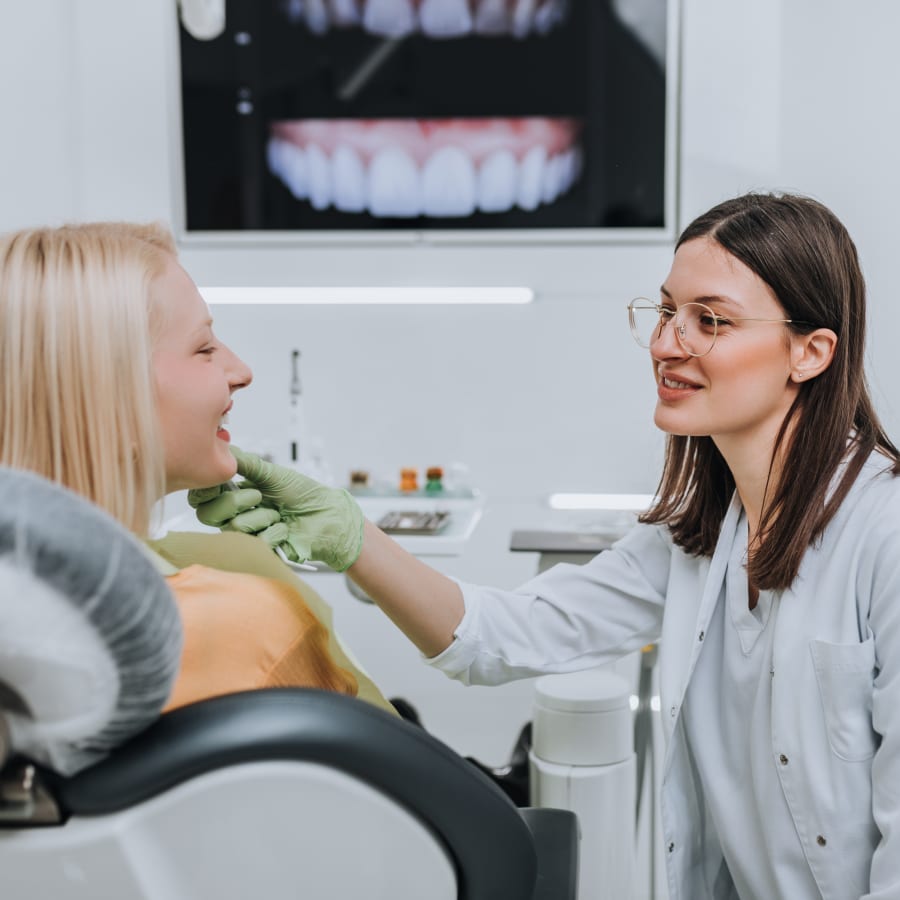 Dentist examining a patient's teeth with a dental X-ray displayed in the background.
