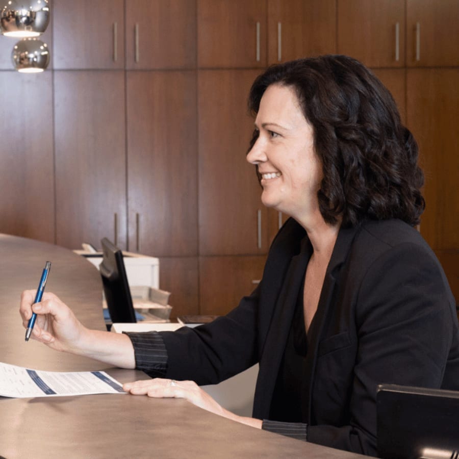 A dental assistant is smiling brightly as she passes someone a clipboard.