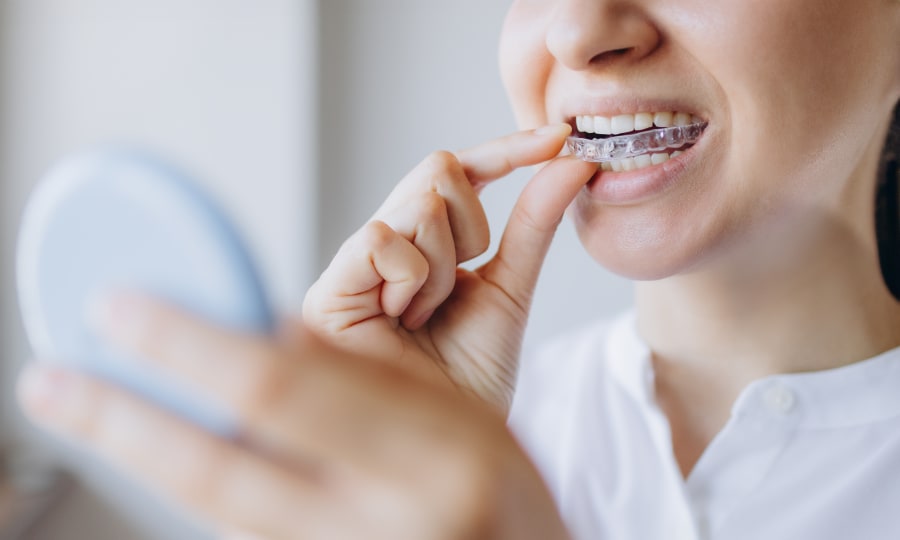 Woman wearing a white top removing her clear aligners.