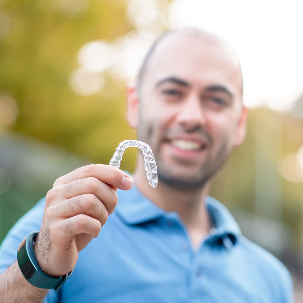 Man wearing a blue top is holding Invisalign aligners.
