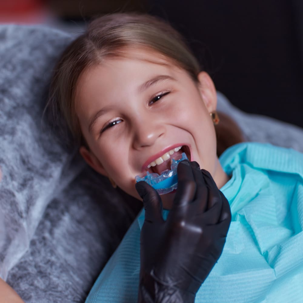 Young boy with blonde hair inserting a custom mouthguard into his mouth.