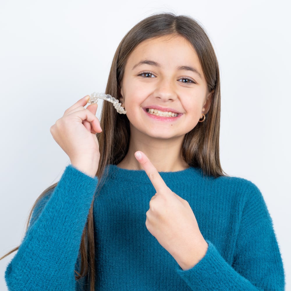 A young girl holds a retainer in front of her mouth.