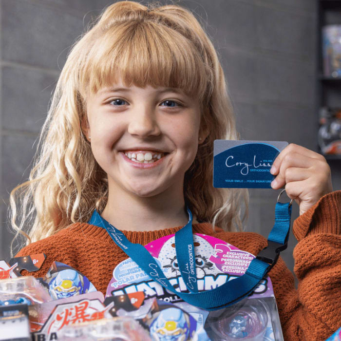 A young girl holding up prizes and her Cory Liss Orthodontics lanyard